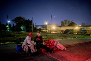 Homeless people sitting and talk at a roadside on a Sunday night.