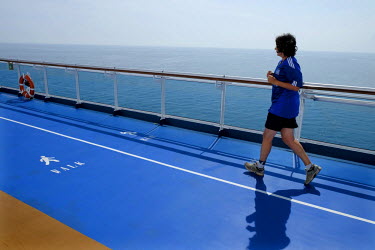 A tourist jogging round the exercise track on board a luxury cruise liner. These vast ships carry thousands of passengers and thousands more staff to cater for their every need.