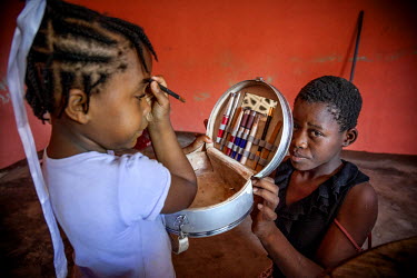 Teacher's daughter Bubu (5) applies make-up while Judeline, a 12 year old 'restavek', holds the child's make-up box. 'Restaveks' are children whose impoverished parents have indentured them into domes...