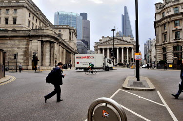 A man checks his phone as he crosses Bank Junction (Bank of England at left, Royal Exchange at centre) in the City of London. A truck belonging to a data shredding company is passing behind him.