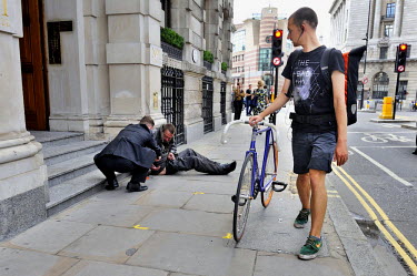 A cycle courier looks on as a young businessman crouches down to offer a homeless man, begging on Cornhill, in the City of London.