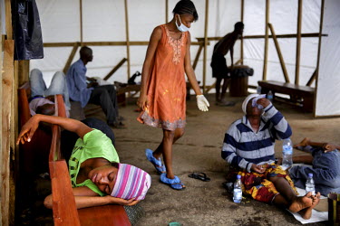 Isha Kamara (orange dress), who is symptom free, assists eight members of her family, the Fofana-Kamaras, who have become ill with ebola-like symptoms and are lying inside a tent outside the Connaught...