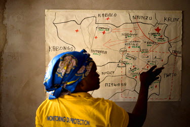 Marie, a protection monitor with UNHCR partner organization IEDA, points out various IDP sites on a hand drawn regional map at IEDA's office in Manono. Dubbed the 'Triangle of Death' due to frequent a...