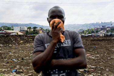 A relative of Isafu Bagua, recently deceased, holds a cloth to his face at the King Tom Cemetery. Due to the rapid increase in burials the cemetery is being enlarged and parts of a nearby rubbish dump...