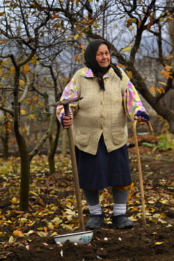 Elizaveta Donciu (82), a former collective fruit farm worker outside with a walking stick and a hoe.