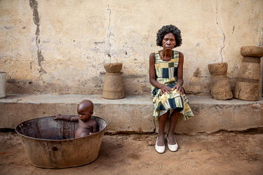 Traditional healer Elena Jakson outside her house with her one year old granddaughter Marbel sitting in a tin bath beside her.