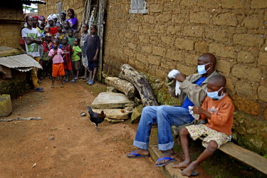 Villagers watch on as Siafa Sherif (8) and his dad, Sekou Sherif, put on barrier gloves. They both have the symptoms of ebola and are being transfered to Macenta for treatment. Prior to this negotiate...