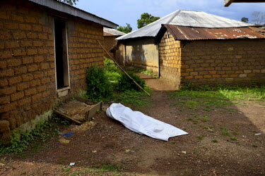 A body, lying in the open outside a house, has been covered with a tarpaulin by visiting Red Cross workers. The village, isolated in the mountainous wooded Forest Region of Guinea, finally opened up t...