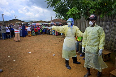 A Red Cross worker, dressed in full PPE (personal protection equipment), directs one of a group of people with Ebola symptoms to a vehicle. The sick villagers made themselves known to visiting medical...