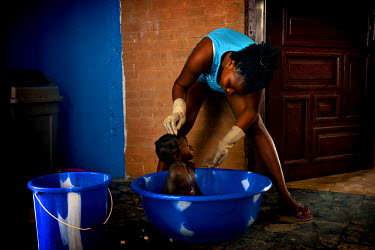 A caretaker at the ICC (interim care centre) cools down Mary who has a high fever, while waiting for an ambulance to transfer the 15 month old girl to the Ebola Treatment Unit. The caretakers are all...