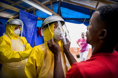 Two Western aid workers are helped into their PPE (Personal Protection Suits) by two locally employed staff at an Ebola treatment centre.