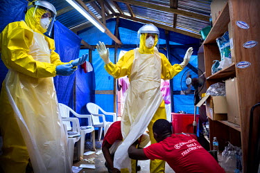 Two Western aid workers are helped into their PPE (Personal Protection Suits) by two locally employed staff at an Ebola treatment centre.