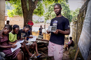 A group of students follow a lesson being transmitted by radio. As a result of the Ebola crisis all schools have been closed. Children are now taught via a daily radio broadcast where special educatio...