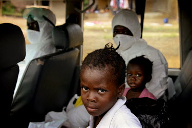 Phoebe,6, and her sister Mary, 15 mths, travelling, with a medical worker (dressed in personal protection equipment), to the ICC (interim care centre) in Monrovia. Phoebe (6) and Mary (15 months) are...
