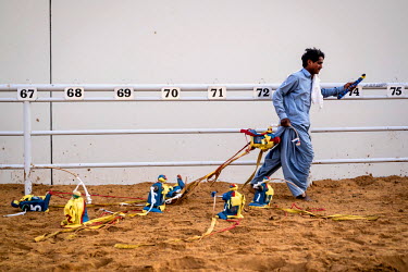A race track worker takes the robot jockeys, after testing, to be attached to the camels before the start of a race.