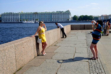 Two tourists take photos of each other on the Neva River front opposite the Hermitage.