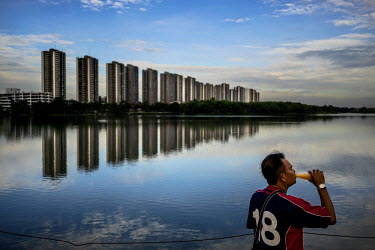 A man drinks from a bottle across the way from Victoria Lake View Condominiums on the shores of a man made lake. ~This project started off 17 years ago but didn't survive the economic crisis of the 90...