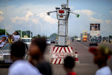 An 8 foot tall, solar powered humanoid traffic robot equipped with a rotating chest and video cameras controls and monitors traffic on a busy road in Kinshasa.