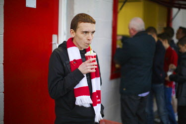 A fan drinks half time refreshments while people queue for pies behind.Hamilton is a small town of 40,000 with a stadium that fits just 6,000 people. The club is 140 years old and is the only team in...