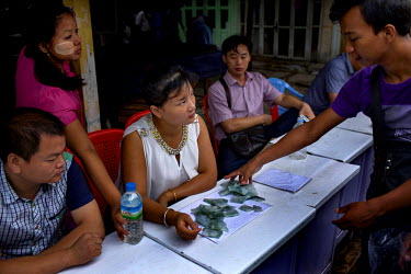 Chinese buyers (seated) are shown pieces of cut jade by a Burmese trader (right) at the Mandalay Jade market.