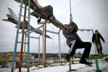 Children swinging on ropes in a playground in Norilsk, a city built by prisoners of the Gulag Norilsk and one of the most polluted cities in the world. Above them two fighter planes have been installe...