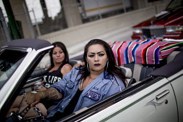 Hispanic women in a car at the Voodoo Kings Car Club's Brett Bennett and Jorge Flores during a flame throwing contest at the 4th Annual Slow & Low: Chicago Community Lowrider Festival.