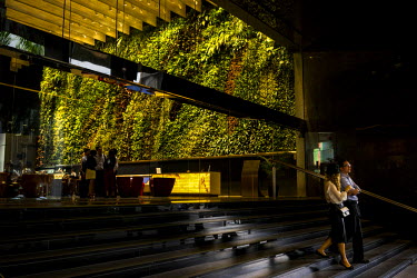 People walk past the 'Rainforest Rhapsody', a 2000 square foot indoor vertical garden installed in the lobby of Six Battery Road that contains 120 plant species. In Singapore, skyrise greenery helps t...