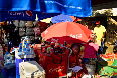 A woman selling cold soft drinks is one of several vendors on a busy roadside.