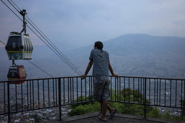 A man stands and looks at cable cars going past at a lookout point near the Santo Domingo metro-cable in Comuna 1, the first of several transformation projects in Medellin which connects the city's po...