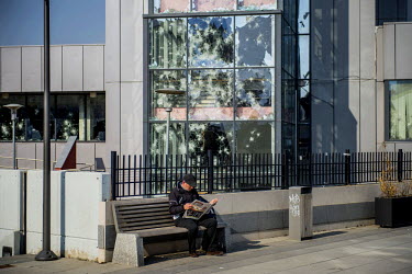 A man reads a newspaper in front of the smashed windows of a government building damaged by rioters in protests against the Kosovan government in January 2015.