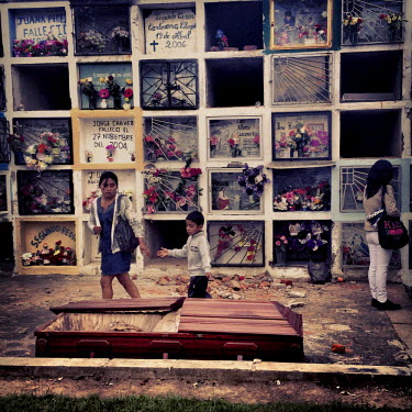 A woman and a boy walk by an empty coffin that was left in the cemetery of Tumbaco on Dia de los Muertos (Day of the Dead).
