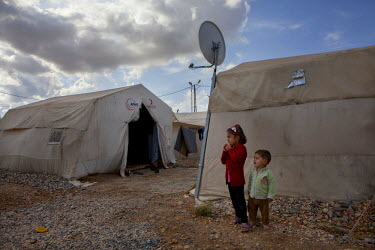 Two children standing beside tents at the Nzip refugee camp, established in Southern Turkey, for people displaced by the war in Syria.