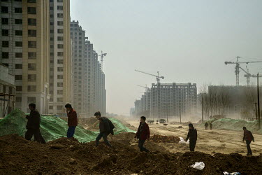 Workers walk on a road running through a new housing developement that is being built on top of reclaimed farmland. In a move to increase the size of the middle class and boost demand, the government...