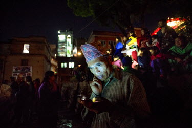 The face of an older Nepali man wearing a traditional 'topi' hat is illuminated by his cell phone while he text messages at the Bisket Jatra festival in Bhaktapur, one of the three city state's in Nep...