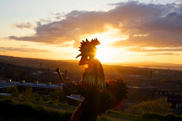 A man in a bird costume is silhouetted against the setting sun with a view of Edinburgh in the background as seen from Carlton Hill, the scene of the annaul Beltane Fire Festival.  The Beltane Festiv...