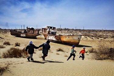 Boys playing in the dunes near the 'graveyard of ships', a group of rusting trawlers, abandoned on the former shore of the Aral Sea. The town is within the catchment area of the Amu Darya river delta...
