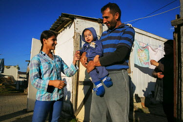 A young couple and their baby standing outside the converted container which is their home.