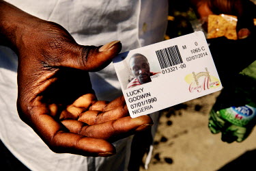 A Nigerian migrant shows his identity card issued by Casa Mineo. The Mineo centre for asylum seekers in an old residential compound originally built for the families of US military personnel. It was a...