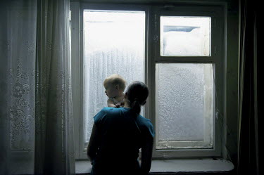 A woman holds her child which is standing on a window sill while looking out at a wall of snow that has accumulated in front of their apartment block in Norilsk.  The city is covered in snow for aroun...