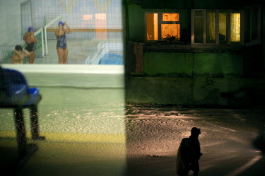 Swimmers in a swimming pool are reflected in a window through which people walking through the snow are visible. Since outside activities are very much restricted due to the weather indoor sports are...