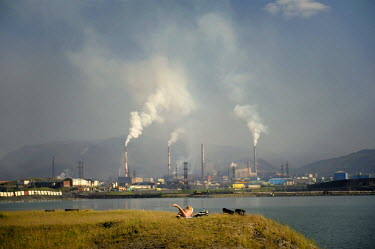 A woman sunbathes on a patch of green overlooking a lake near the city of Norilsk with the smoke stacks of nearby factories visible in the background.  The city has very few green spaces and people ne...