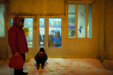 A man and a child wait for a bus outside a small grocery shop in Norilsk. A girl and a woman are waiting inside. Many shops double up as warm bus shelters in Norilsk where temperatures average -30C in...
