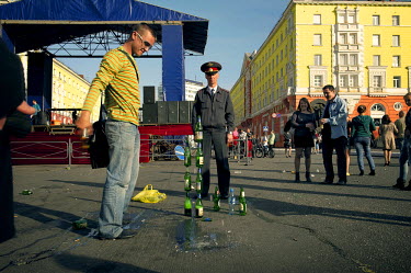A man tries to balance bottles of beer on top of each other on a square in Norilsk, watched over by a policeman, during the polar summer when the sun doesn't set for 45 days.   The city of Norilsk, in...