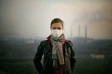 A portrait of a woman wearing a mask against polluted air against the backdrop of a Norilsk cityscape. The air is particularly polluted during the summer. Every year, the metallurgical industry emits...