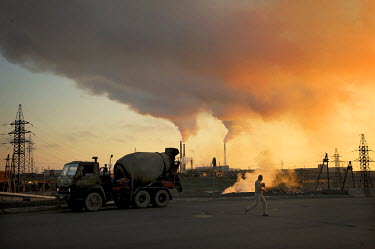 A man walks past a cement mixer with industrial smoke stacks visible in the background on day during the polar summer when the sun doesn't set properly for around 45 days.  The city of Norilsk, in the...