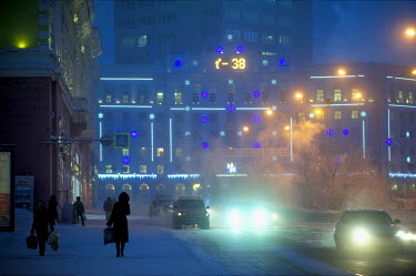 Pedestrians walk on the pavement and cars pass on a cold night in Norilsk. A temperature display shows -38C. The city is one of the coldest in the world with winter temperatures averaging -30C. Around...