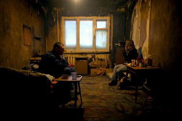A man sits on his bed in a run down hostel in Norilsk. A woman sits on a chair near him. In order for citizens of former Soviet republics to come and live in the city they are required to get special...