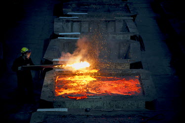 A worker handles a glowing metal rod next to a large industrial container full of molten metal at one of the smelters in Norilsk.  The complex consists of three plants - the nickel plant, the copper p...