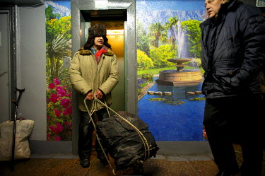 A man wheels a bag on a trolley out of a lift in a residential apartment block in Norilsk. Many entrance halls of these blocks are decorated with brightly coloured images of summer scenes and tropical...