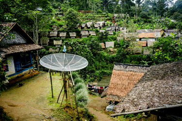 A satellite dish sits in the courtyard of a small home in the village. In the distance are rice barns that store the harvest from past seasons. Much of the village life here continues to be in the Ada...
